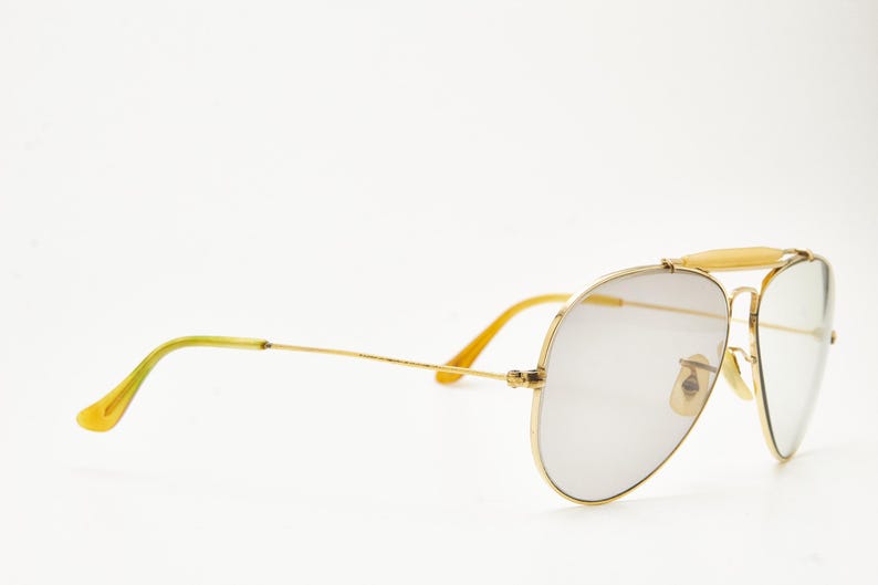 Puede incluir: Gafas de sol de aviador con montura dorada y lentes grises. Las gafas tienen doble puente y puntas de patillas amarillas. Las lentes tienen forma de l&aacute;grima. La montura es de color dorado brillante.
