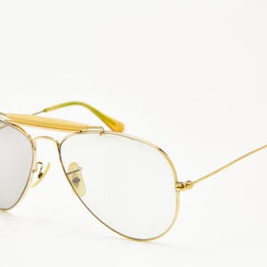 Puede incluir: Gafas de sol aviador con montura dorada y lentes espejadas plateadas. Las gafas de sol tienen una barra de puente y patillas con detalles amarillos y verdes. Un accesorio de gafas cl&aacute;sico.