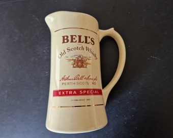 Puede incluir: Una jarra de cerámica blanca con asa, con el logotipo de Bell's Old Scotch Whisky. El logotipo incluye el nombre de la marca, un escudo de armas y el texto "Arthur Bell & Sons plc, Perth Scotland, Extra Special, Established 1825."