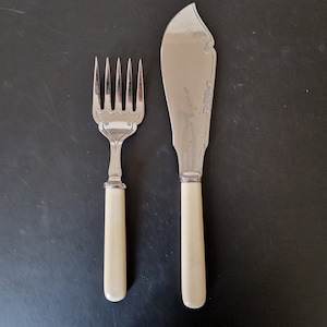 Puede incluir: Un juego de cubiertos plateados con mangos de color marfil. El juego incluye un tenedor y un cuchillo para mantequilla.