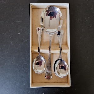 May include: A set of three silver spoons in a white box. The spoons are all polished and have a reflective surface. The spoons are arranged in a row, with the largest spoon in the centre and the two smaller spoons on either side.