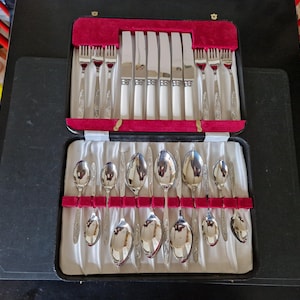 May include: A black case with a red velvet interior contains a set of silver cutlery. The cutlery includes knives, forks, and spoons.