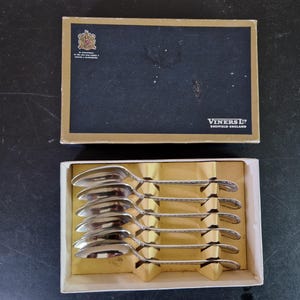 Puede incluir: Un juego de seis cucharaditas de plata en una caja blanca con tapa negra y dorada. La tapa tiene el texto "Viners Ltd. Sheffield England".