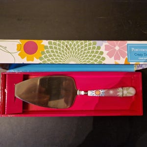 以下が含まれることがあります： Portmeirion Crazy Daisy Cake Sliceシリーズのケーキサーバー。 サーバーはステンレス鋼の刃と、花柄の装飾的なハンドルが付いています。 花柄の蓋が付いたピンク色の箱に入っています。