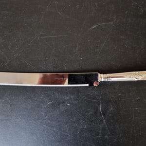 May include: A silver cake knife with an ornate handle and a serrated blade.