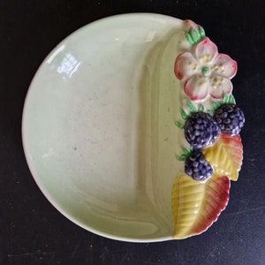 Puede incluir: Un plato de cerámica verde pálido con una sección dividida. El plato está decorado con un diseño en relieve de una flor rosa con centro amarillo y moras con hojas verdes.
