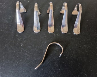 May include: Six silver metal hooks with a rounded shape and a slight curve. The hooks are arranged in a row on a dark surface. There is a single silver metal hook with a similar shape but a different curve in the bottom right corner of the image.