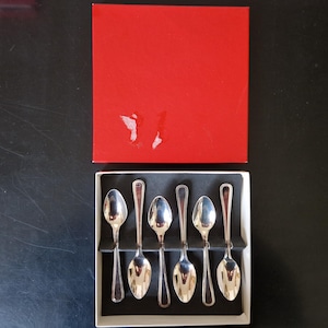 Puede incluir: Un juego de seis cucharas de plata en una caja blanca con tapa roja. Las cucharas tienen un diseño clásico con cuencos redondeados y mangos largos y delgados. La caja es rectangular.