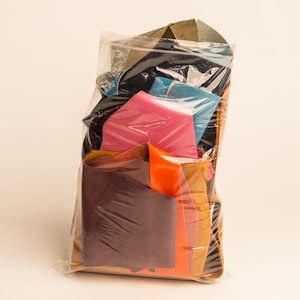 Könnte beinhalten: Ein klarer Plastikbeutel gefüllt mit bunten Stoffresten. Die Stoffe sind in verschiedenen Farben, darunter Rosa, Blau, Orange, Braun und Schwarz. Der Beutel ist versiegelt und der Inhalt ist sichtbar.