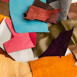Könnte beinhalten: Eine Sammlung farbenfroher Lederreste in verschiedenen Farbtönen, darunter Blau, Rosa, Orange und Braun. Die Stücke sind in einer geschichteten Komposition angeordnet, die die verschiedenen Texturen und Farbtöne des Materials zeigt. Ideal für Bastelprojekte.