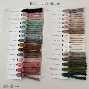 Puede incluir: Una carta de colores Bobbiny Farbkarte con dos tarjetas blancas que contienen muestras de hilo en varios tonos. La tarjeta izquierda enumera colores desde Midnight Dust hasta Mauve, y la derecha desde Pearl hasta Pine Green, con etiquetas.
