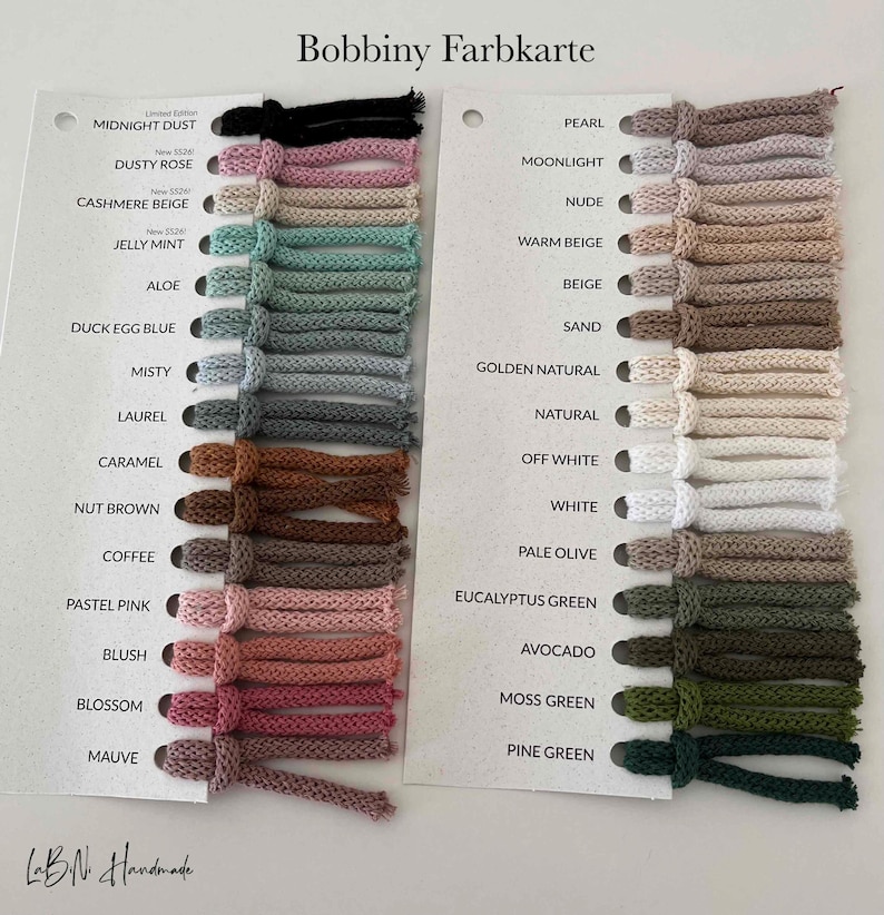 Puede incluir: Una carta de colores Bobbiny Farbkarte con dos tarjetas blancas que contienen muestras de hilo en varios tonos. La tarjeta izquierda enumera colores desde Midnight Dust hasta Mauve, y la derecha desde Pearl hasta Pine Green, con etiquetas.