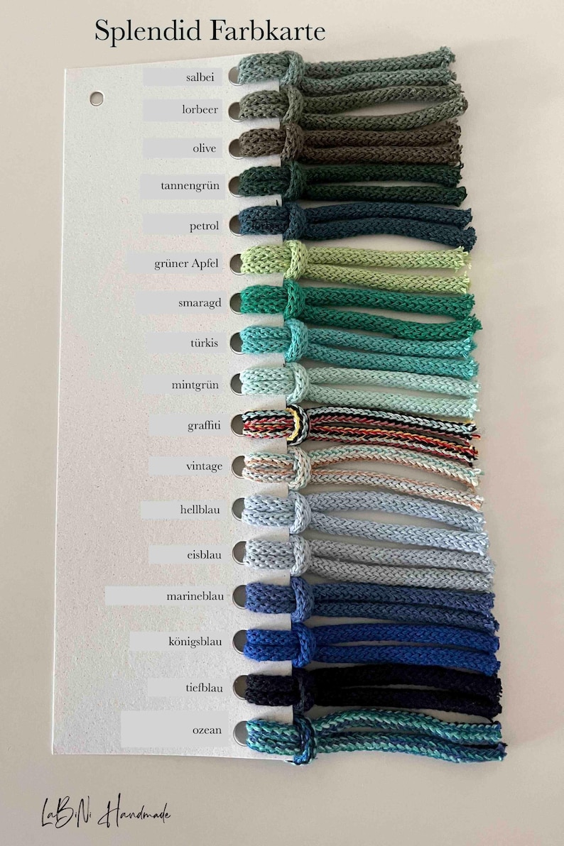 Puede incluir: Una carta de colores titulada Splendid Farbkarte que presenta una fila vertical de diecis&eacute;is muestras de cord&oacute;n trenzado en varios tonos de verde, azul y patrones multicolores. Cada cord&oacute;n est&aacute; anudado a una tarjeta blanca con etiquetas.