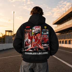 Könnte beinhalten: Ein schwarzer Kapuzenpullover mit einem großen Grafikdruck auf der Rückseite. Das Design zeigt den Formel-1-Fahrer Charles Leclerc in einem roten Rennanzug, einem Rennhelm und einem roten Rennwagen. Das F1-Logo und der Name sind deutlich zu sehen.