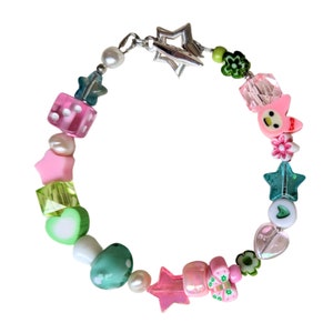 May include: A colorful beaded bracelet with a star charm, pink and green dice, hearts, stars, and flowers. The bracelet is made of plastic and metal.