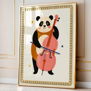 May include: A framed art print featuring a cartoon panda playing a pink cello. The panda is black and white with a brown vest. The background is cream-colored with gold stars and a decorative border. The frame is gold.