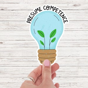 Op de afbeelding: Een lichtblauwe sticker in de vorm van een gloeilamp met een groene plant die erin groeit. De sticker heeft de tekst "PRESUME COMPETENCE" rond de lamp.