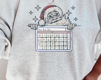 May include: A grey sweatshirt featuring a graphic of Santa Claus peeking over a computer screen with the text "ho ho ho" and a grid of emojis.