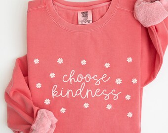 Könnte beinhalten: Ein korallenrosa Sweatshirt mit dem Text "choose kindness" in weißer Schrift, umgeben von weißen Gänseblümchen. Das Sweatshirt hat einen Rundhalsausschnitt und lange Ärmel.