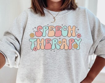 May include: A gray sweatshirt with the text "SPEECH THERAPY" in colorful retro-style lettering with flowers and stars.