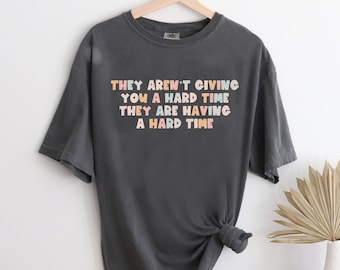 May include: A dark grey t-shirt with the text "They aren't giving you a hard time they are having a hard time" printed in colourful letters.
