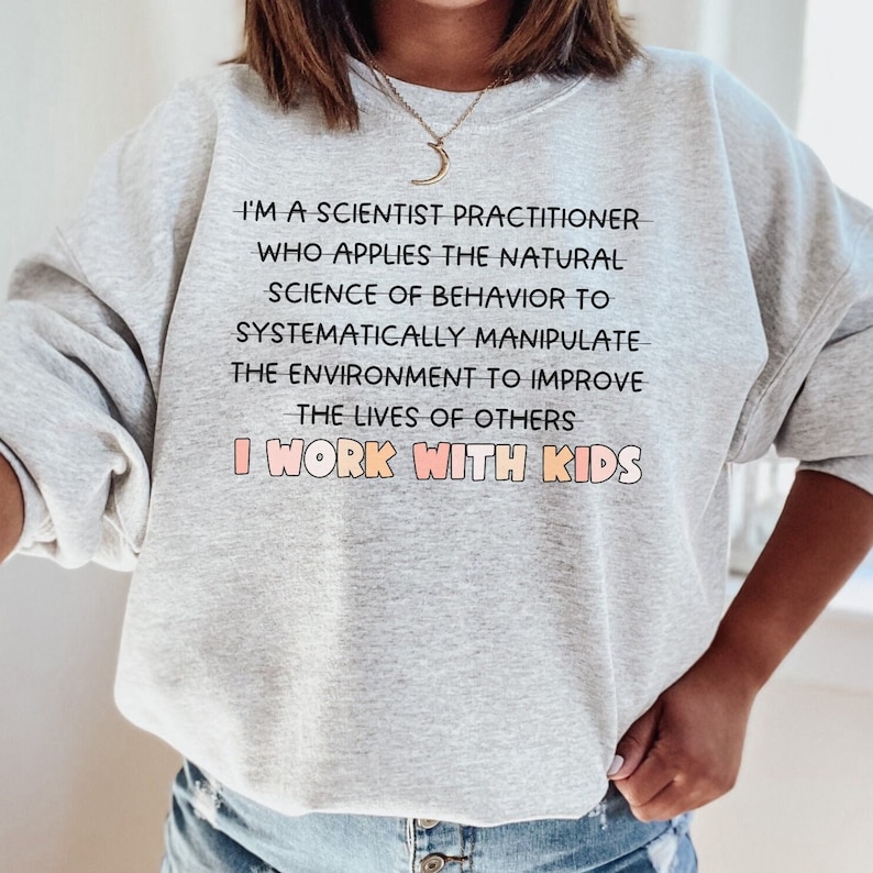 May include: Gray sweatshirt with the text "I'm a scientist practitioner who applies the natural science of behavior to systematically manipulate the environment to improve the lives of others I work with kids".