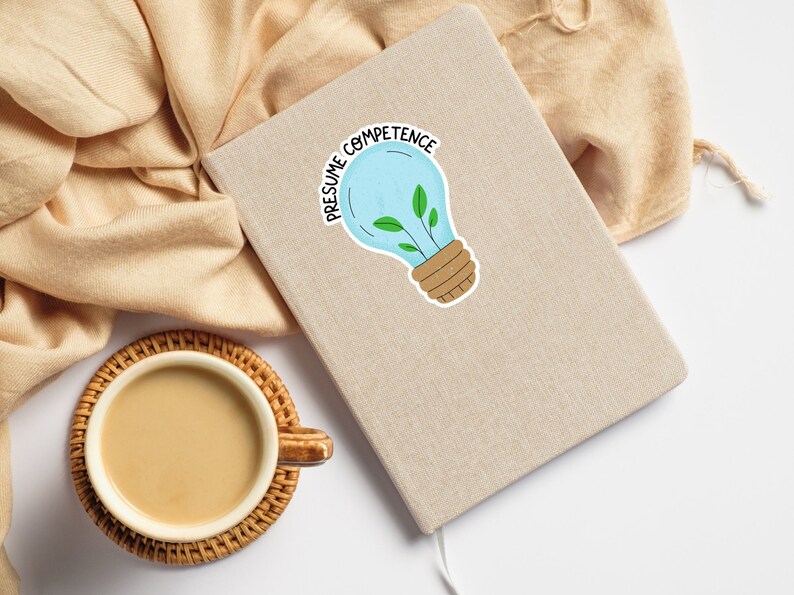 Op de afbeelding: Een lichtbruin notitieboekje met een lichtblauwe sticker in de vorm van een gloeilamp waarop "Presume Competence" staat. De gloeilamp heeft een groene plant die erin groeit.
