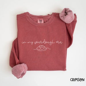 Peut inclure: Un sweat-shirt marron avec le texte "in my sourdough era" et un dessin simple d'une miche de pain.