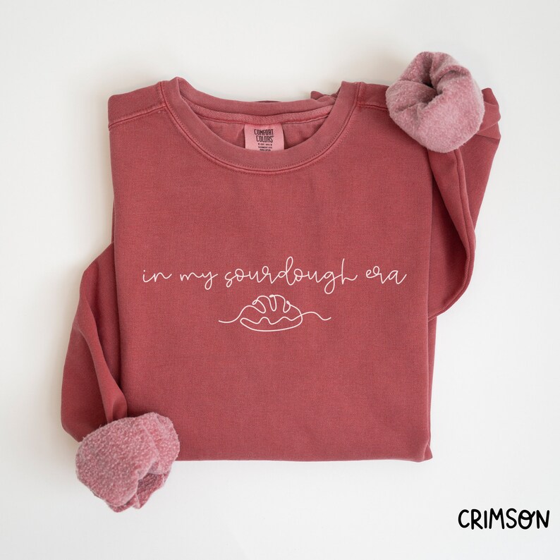 Peut inclure: Un sweat-shirt marron avec le texte "in my sourdough era" et un dessin simple d'une miche de pain.