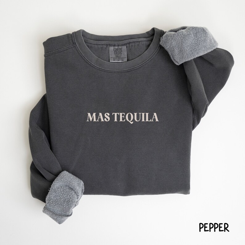 May include: A dark gray sweatshirt with the text "MAS TEQUILA" in white lettering. The sweatshirt has a fleece lining and is made of a soft, comfortable material.