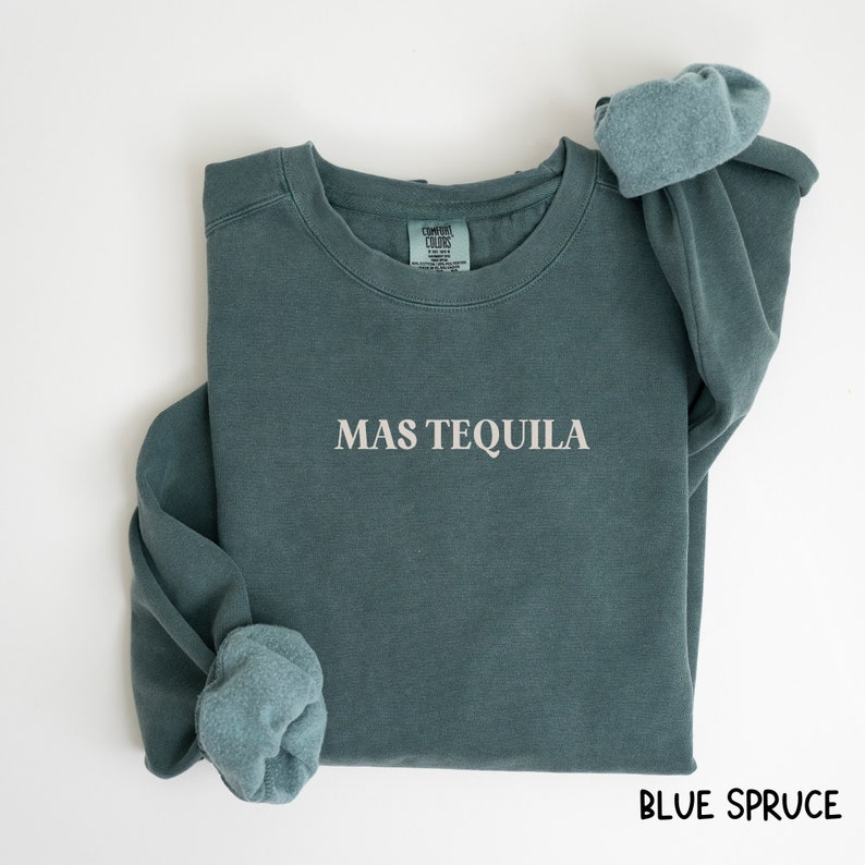 May include: A blue sweatshirt with the text "MAS TEQUILA" in white lettering. The sweatshirt is folded and the sleeves are rolled up. The background is white.