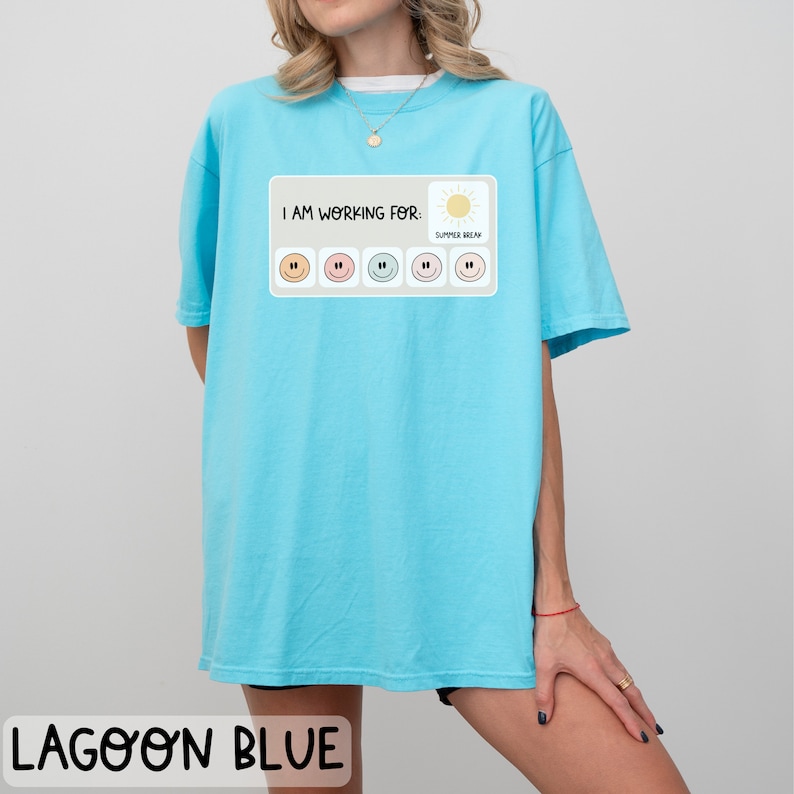 May include: A light blue t-shirt with a graphic that says "I am working for: Summer Break" with a series of smiley faces in different colors.
