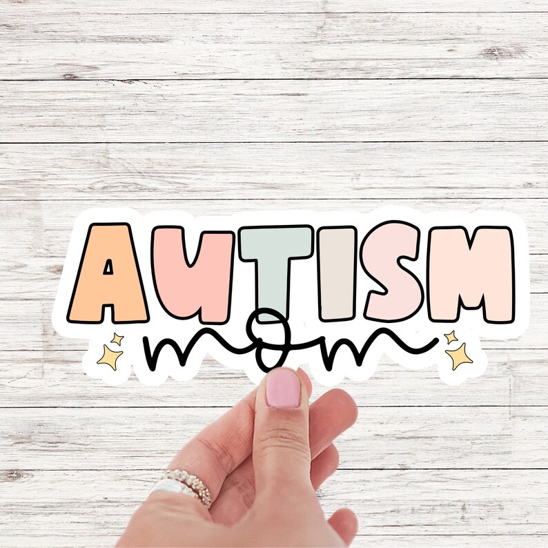 May include: A white sticker with the word "AUTISM" in rainbow colours and the word "mom" written in black cursive underneath. The sticker has two small yellow stars on either side.