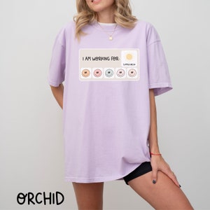 May include: A lavender t-shirt with the text "I am working for: Summer Break" and a graphic of a sun and six smiley faces.