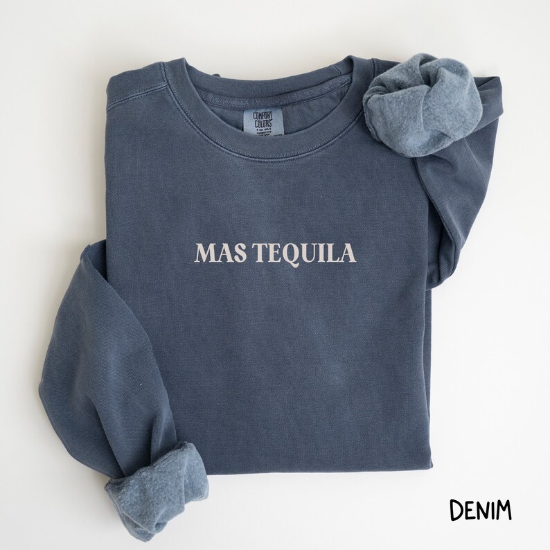 May include: A dark blue sweatshirt with the text "MAS TEQUILA" in white lettering. The sweatshirt is made of a soft, comfortable fabric and has a relaxed fit.