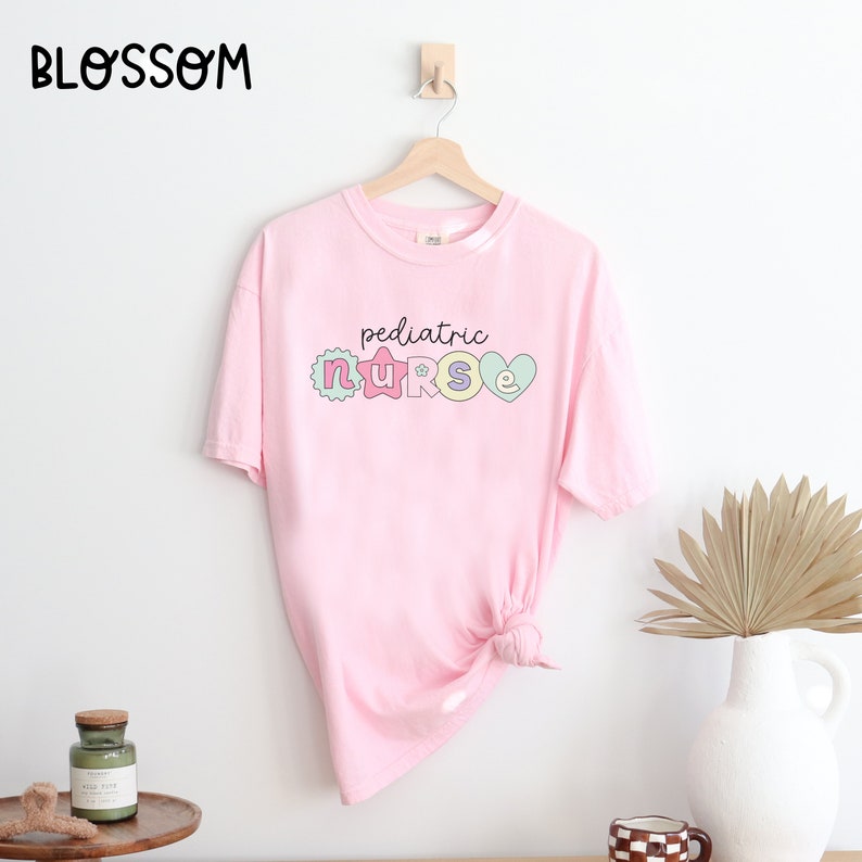 May include: Pink t-shirt with the text "pediatric nurse" in colorful letters with a star and heart design.
