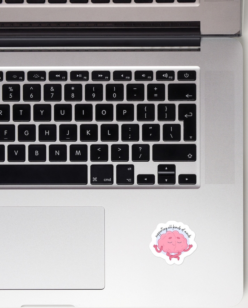 May include: A pink brain sticker with a smiling face meditating with the text "supporting all kinds of minds".