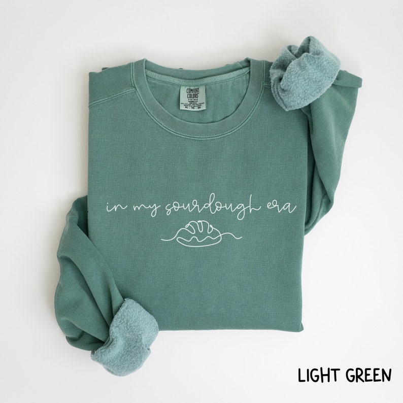 Peut inclure: Sweat-shirt vert clair avec le texte "in my sourdough era" et un dessin simple d'une miche de pain.