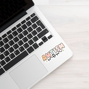 May include: A laptop computer with a sticker that says "AUTISM MOM" in colourful letters with stars.