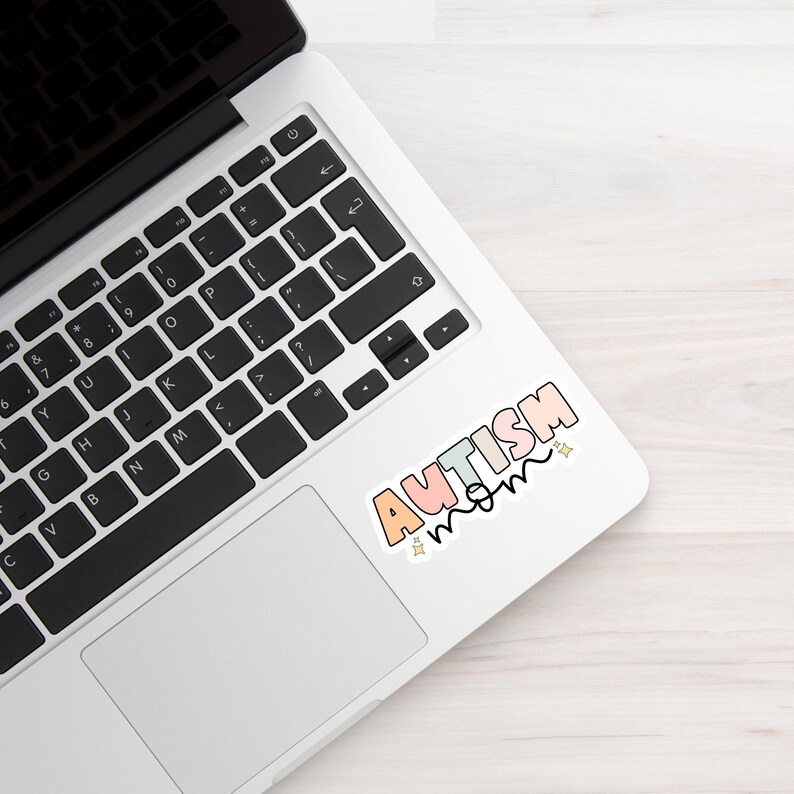 May include: A laptop computer with a sticker that says "AUTISM MOM" in colourful letters with stars.