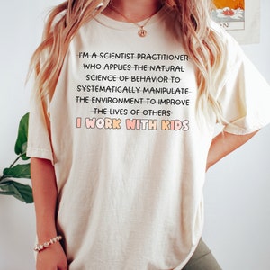 May include: A white t-shirt with a black text graphic that reads "I'm a scientist practitioner who applies the natural science of behavior to systematically manipulate the environment to improve the lives of others I work with kids."