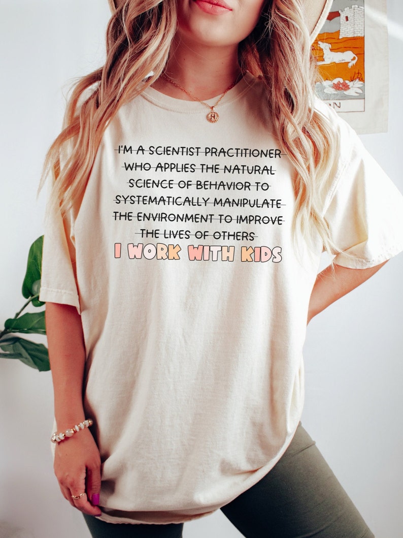 May include: A white t-shirt with a black text graphic that reads "I'm a scientist practitioner who applies the natural science of behavior to systematically manipulate the environment to improve the lives of others I work with kids."