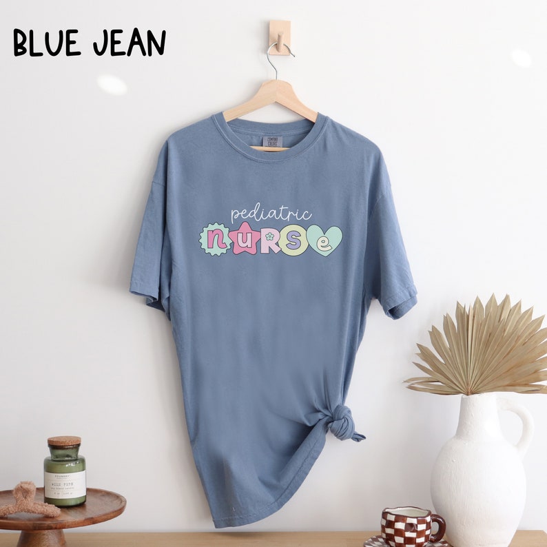 May include: A light blue t-shirt with the text "pediatric nurse" in colorful letters. The letters are decorated with stars and hearts.