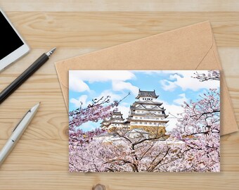 May include: A white Japanese castle with a blue tiled roof surrounded by pink cherry blossoms. The castle is set against a blue sky with white clouds.