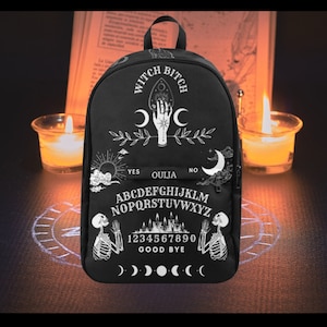 Op de afbeelding: Zwarte rugzak met een wit ontwerp met een Ouija-bord, een halve maan en de tekst "Witch Bitch".