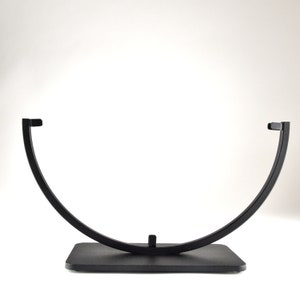 May include: A black metal stand with a curved top and a rectangular base. The stand is designed to hold a round object, such as a plate or a bowl.