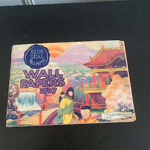 Puede incluir: Un catálogo vintage "Blue Seal Wall Papers 1927". La portada presenta una colorida ilustración de un paisaje japonés con un puente, figuras con vestimenta tradicional y un templo. El catálogo es de T. Eaton Co. Limited, Toronto, Canadá.