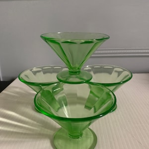 Könnte beinhalten: Set aus vier vintage Dessert-Schalen aus grünem Glas. Die Schalen sind übereinander gestapelt, wobei die oberste Schale die größte ist. Die Schalen haben ein geriffeltes Design und einen klaren Glasfuß.