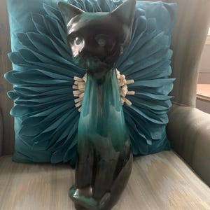 May include: A ceramic cat figurine with a black head and a teal body. The cat is sitting upright with its tail curled around its legs.