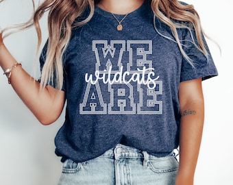 Pode incluir: Uma camiseta azul marinho com texto branco que diz "WE wildcats ARE" em uma fonte de estilo universitário.